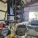 Black outboard powerhead lifted on a chain hoist above a red tool chest, open bay door behind